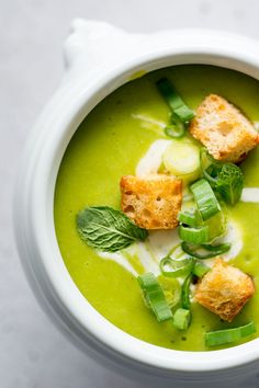 a white bowl filled with green soup and croutons