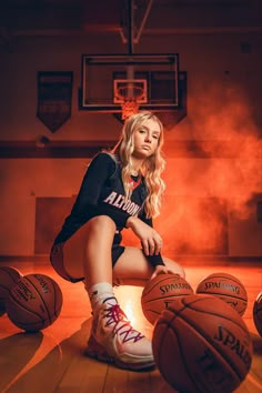 a young woman sitting on top of a basketball court next to some hoops and balls