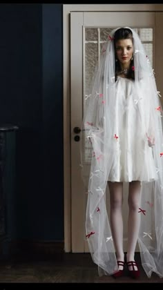 a woman in a white wedding dress with red bows on her head and veil over her face