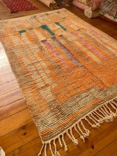 an orange rug with fringes is on the floor in front of pillows and blankets