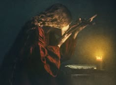 a woman holding a cross in front of a lit candle and looking down at it