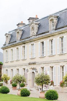 an old house with white shutters and potted plants on the front lawn in front of it