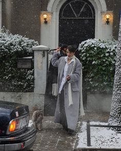 a woman walking down the street in the snow with an umbrella over her head and a cat nearby