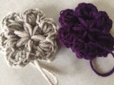 two crocheted flowers sitting next to each other on top of a white surface