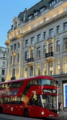 a red double decker bus parked in front of a tall building on the side of a street