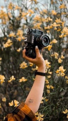 a person holding up a camera in front of yellow flowers