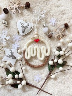 christmas decorations and accessories laid out on a white blanket with snowflakes, pine cones, holly berries, deer head ornament