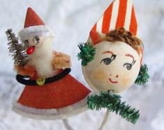 two christmas ornaments are sitting on top of each other, one is wearing a santa claus hat and the other is holding a pine tree