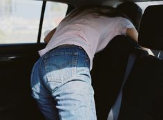 the back end of a woman's jeans in a car with her hand on the rear seat