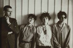 an old black and white photo of four people standing in front of a wooden wall