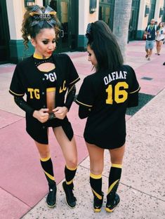 two women dressed in black and yellow outfits on the sidewalk with one holding her cell phone