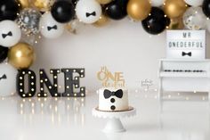 a white cake sitting on top of a table next to a black and gold balloon wall