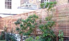 a wooden fence in front of a brick building with trees and bushes growing on it