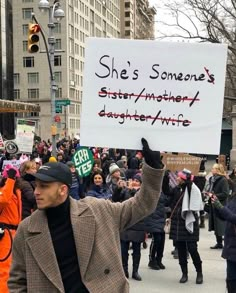 a man holding up a sign that says she's someone's sister / another daughter / wife