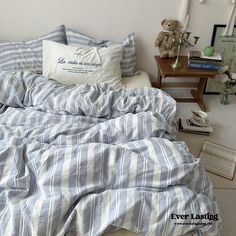 an unmade bed with blue and white striped comforter, pillows and stuffed animals