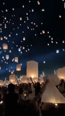 many people are flying paper lanterns in the night sky with lights on their heads and hands