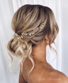 a woman with blonde hair wearing a gold head piece and pearls in her hair is seen from the back