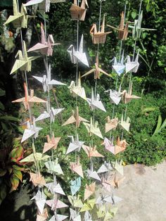 several origami cranes hanging from strings in a garden