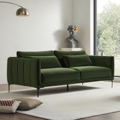 a green couch sitting on top of a white rug in a living room next to a window