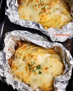 two pieces of foil wrapped in food sitting on top of a black pan filled with meat and cheese covered ravioli