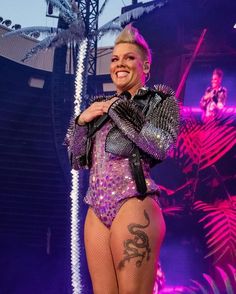 a woman in a purple outfit on stage with her arms around her chest and legs crossed