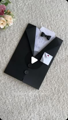 a card with a black suit and bow tie on it, sitting next to flowers