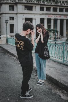 a man and woman standing on the side of a road next to each other with their hands covering their faces