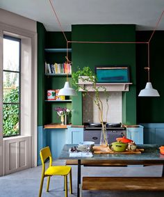 a kitchen with green walls and yellow chairs in front of the counter top, next to a wooden dining table