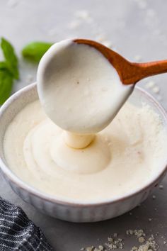 a spoon full of yogurt being held by a wooden spoon over a bowl