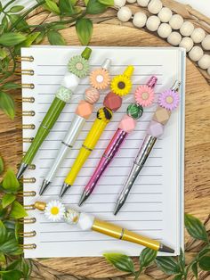 several pens and flowers on top of a notepad next to some eggs with leaves