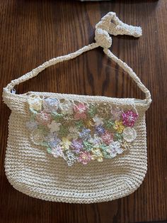 a crocheted purse with flowers on it sitting on top of a wooden table