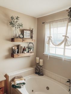 a bath tub sitting under a window next to a shelf filled with candles and other items