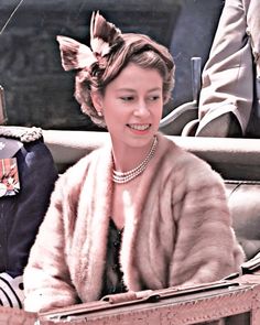 an old photo of a woman in a fur coat and pearls on her head sitting in a carriage