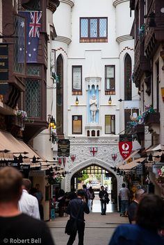 people are walking down an alley way in a city with buildings and flags on the walls