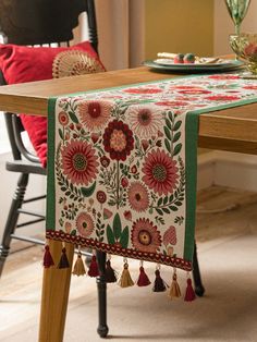 an embroidered table runner with tassels sits on a dining room table in front of a red chair