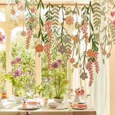 a dining room table with flowers hanging from it's ceiling and cupcakes on the table