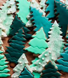 christmas cookies decorated with blue and green icing on a wooden table next to small trees