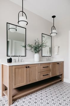 a bathroom with two sinks and mirrors on the wall next to a vase filled with flowers