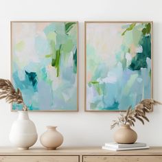 two vases with plants sit on a dresser in front of some paintings hanging on the wall