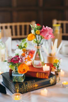 a table topped with books and vases filled with flowers on top of each other