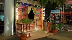 an outdoor stage set up with lights and curtains on it's sides, surrounded by potted plants