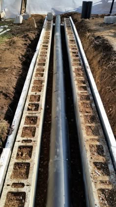 pipes are lined up on the ground in front of some dirt and grass with white tarps behind them