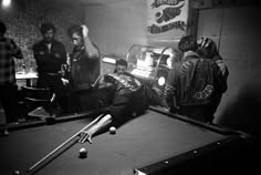 a man laying on top of a pool table next to a group of people standing around