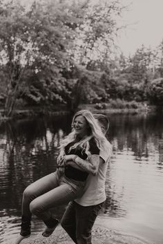 a black and white photo of a woman carrying a man on her back by the water