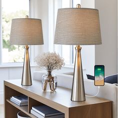 two lamps sitting on top of a wooden table next to a phone and book shelf