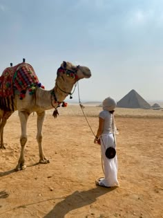 a woman standing next to a camel in the desert