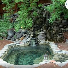 a small pond in the middle of a garden with rocks and water flowing from it