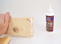 a hand is holding a wood glue bottle next to a piece of wood that has been placed on the table