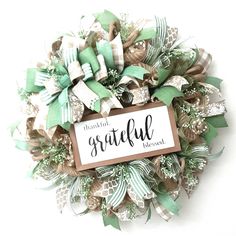 a wreath with the words grateful written on it and green ribbons around it, sitting against a white wall