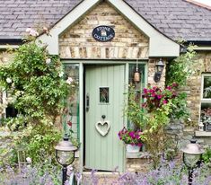 a green door in front of a house surrounded by purple flowers and potted plants